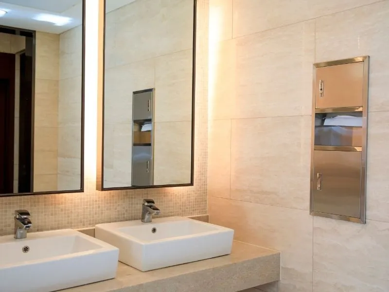 Commercial bathroom with large rectangle mirrors and 2 white sinks near the paper towel dispenser