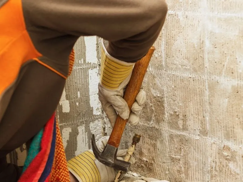 Tiler removing tiles from the wall with a hammer and have gloves in his hand. From Canberra Tiles